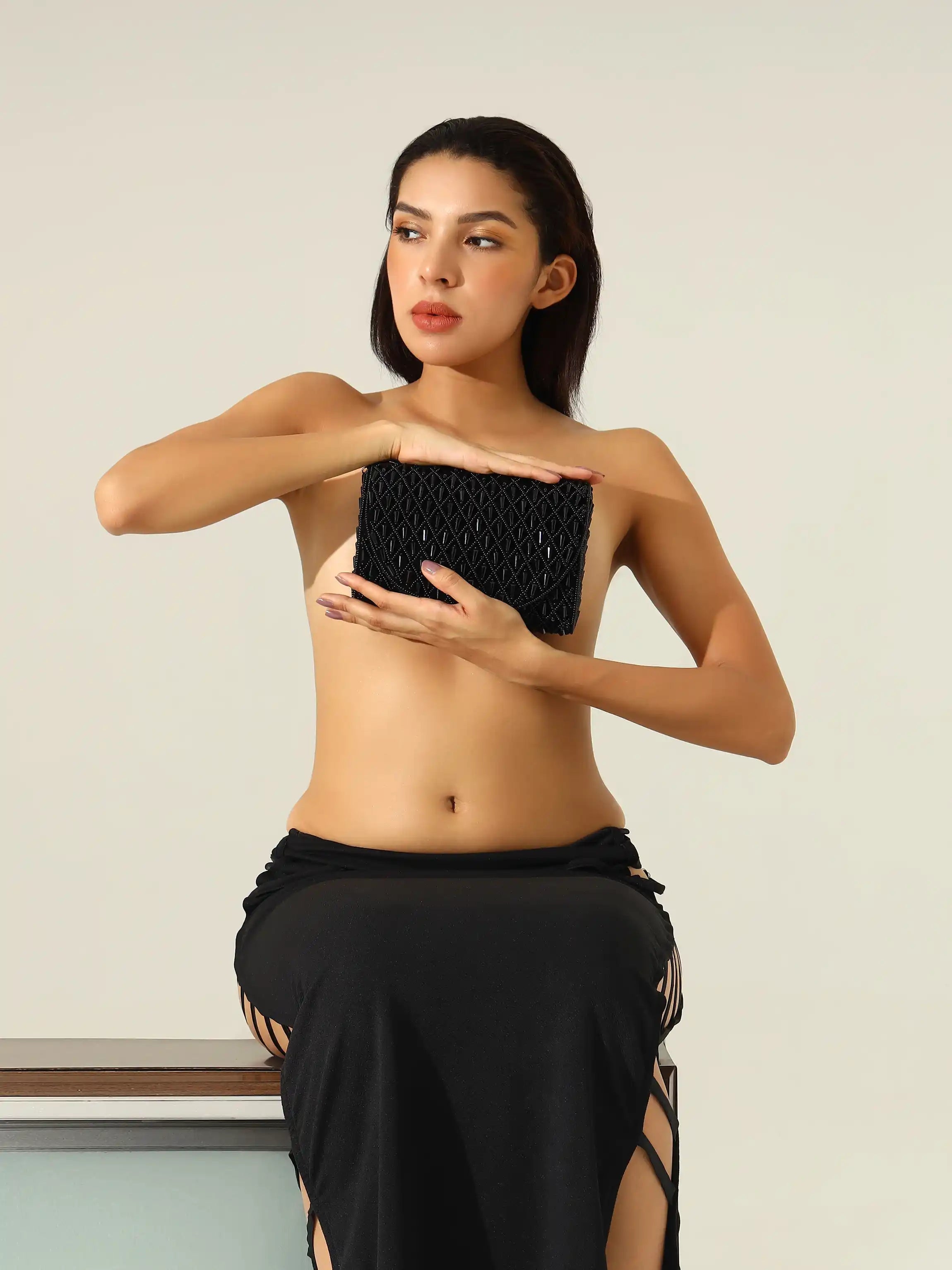 Woman holding a black beaded clutch against a neutral background