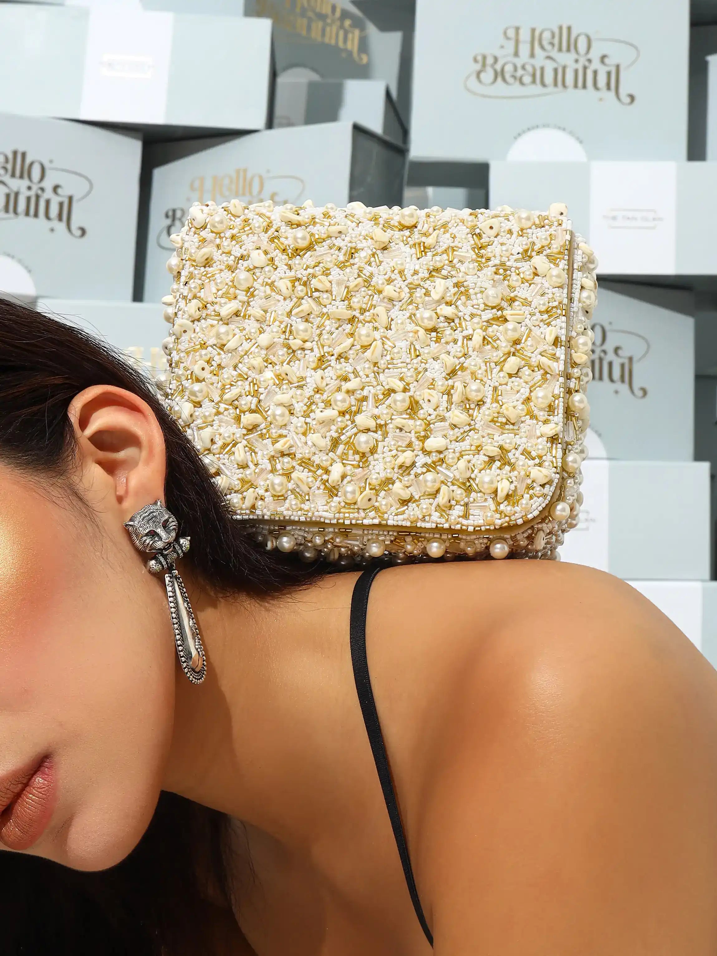 Woman wearing a pearl-embellished clutch with 'Hello Beautiful' boxes in the background