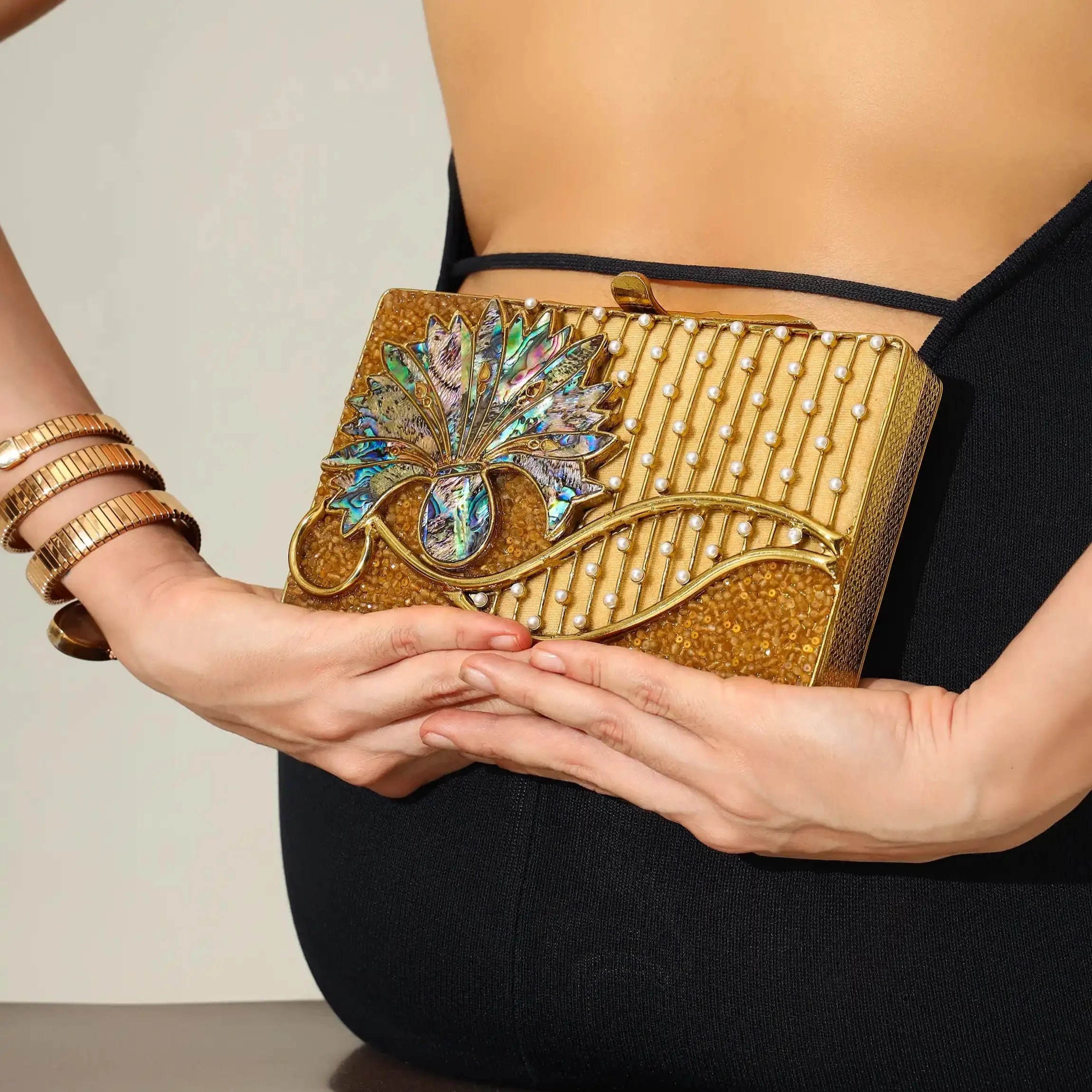 Gold clutch with intricate design held by a person wearing a black outfit.