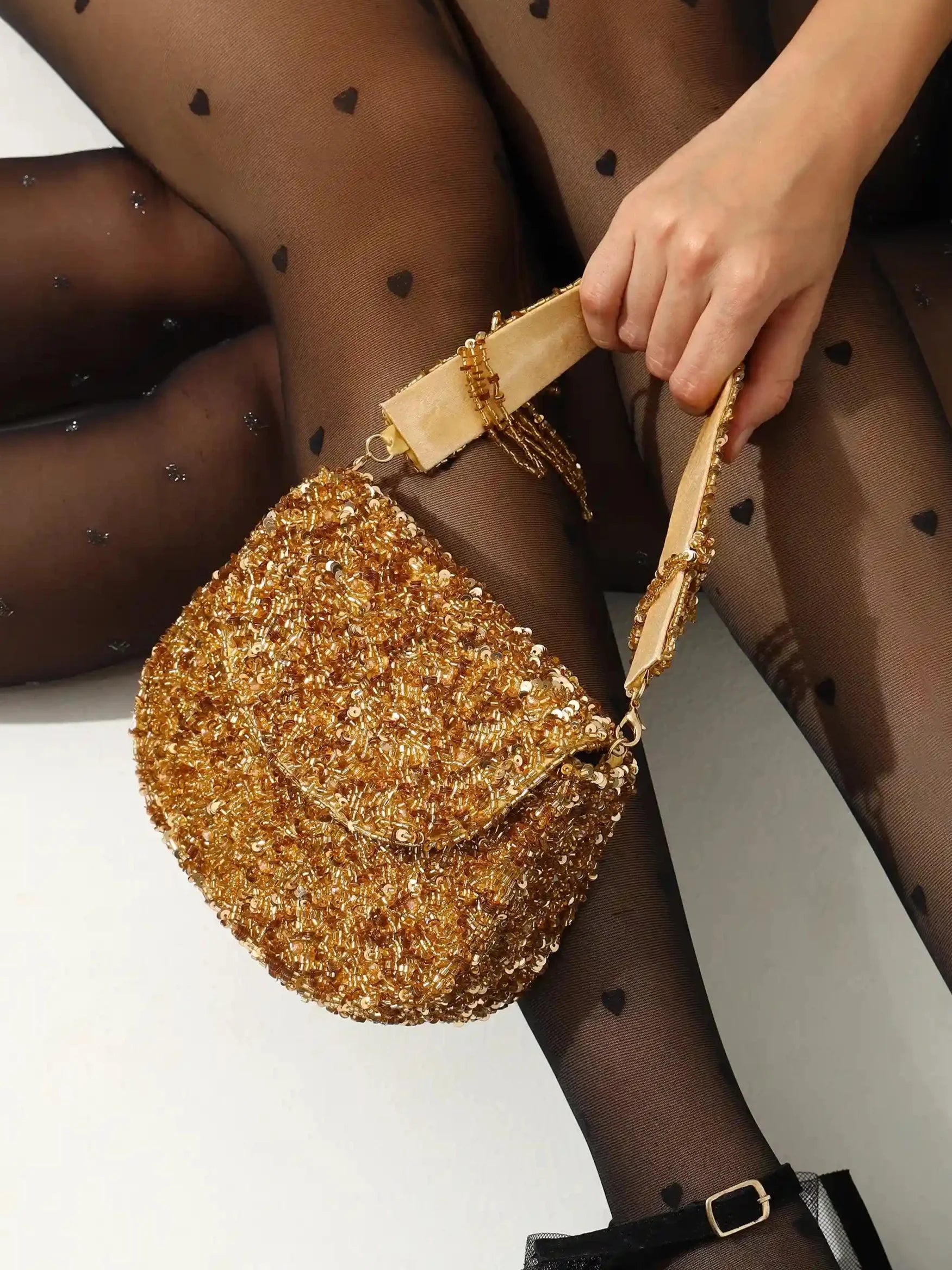 Gold glittery handbag held by a person wearing black tights with heart patterns.