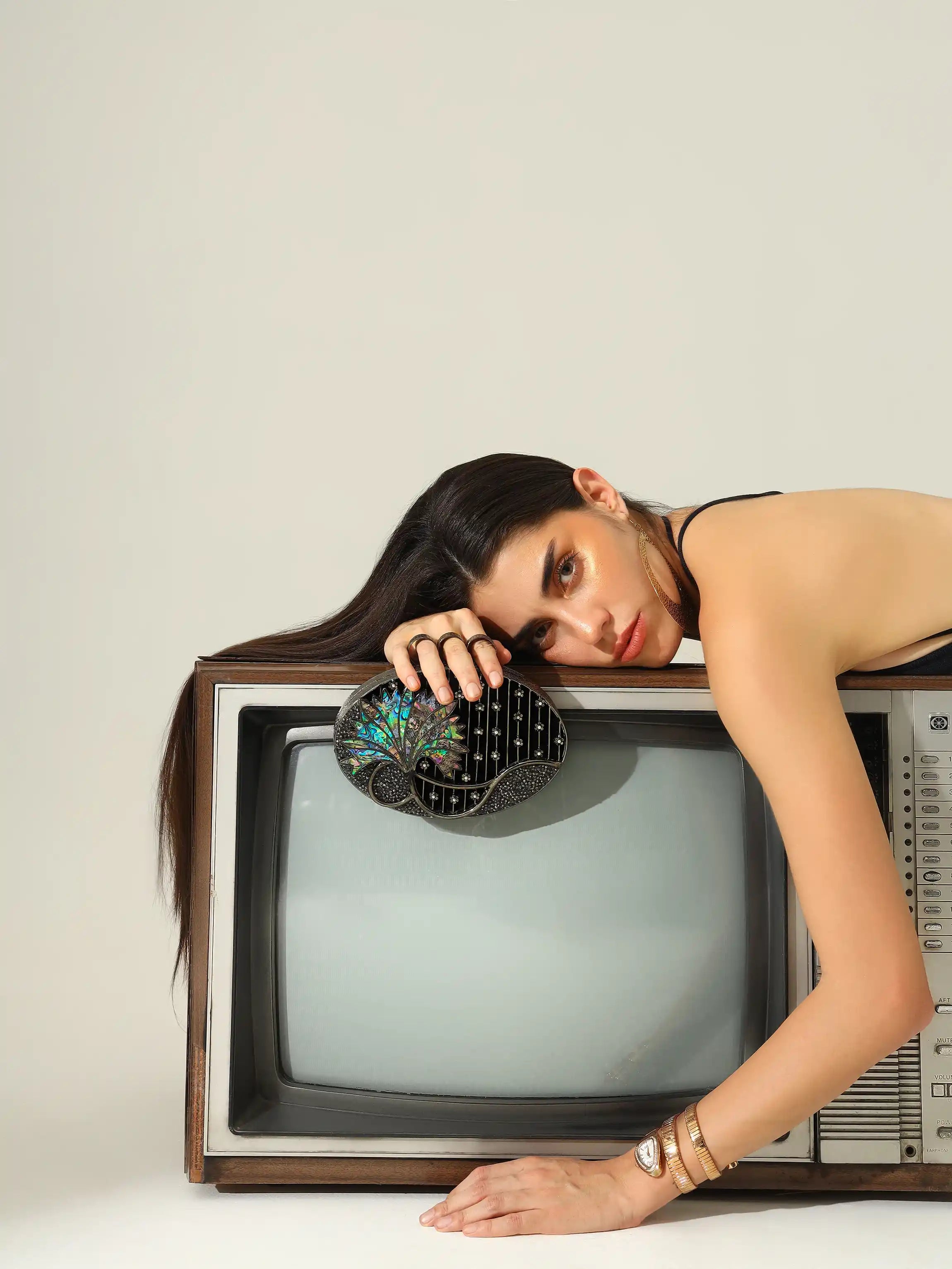 Woman lying on an old television set with a neutral background