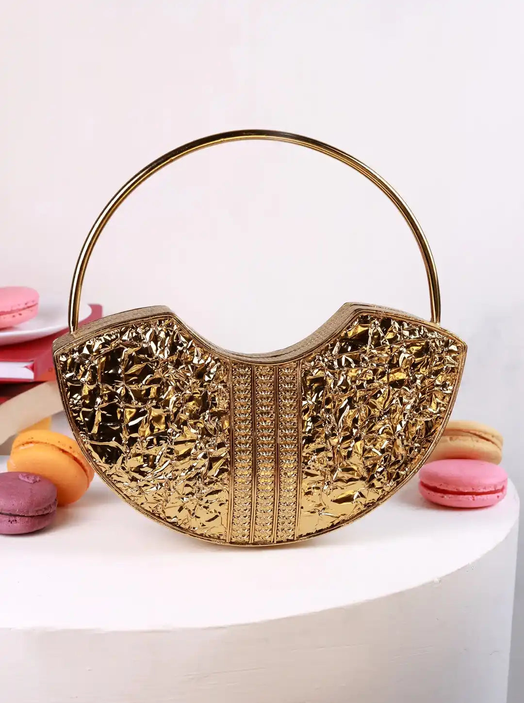 Gold handbag with a unique design on a white surface with colorful macarons.