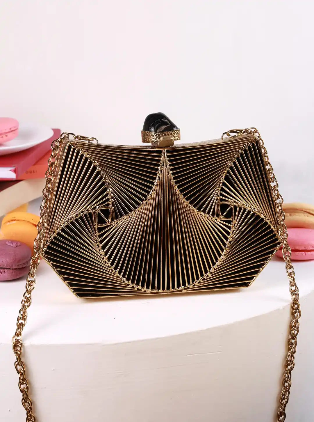 Gold clutch bag with chain strap on a white surface with colorful macarons in the background