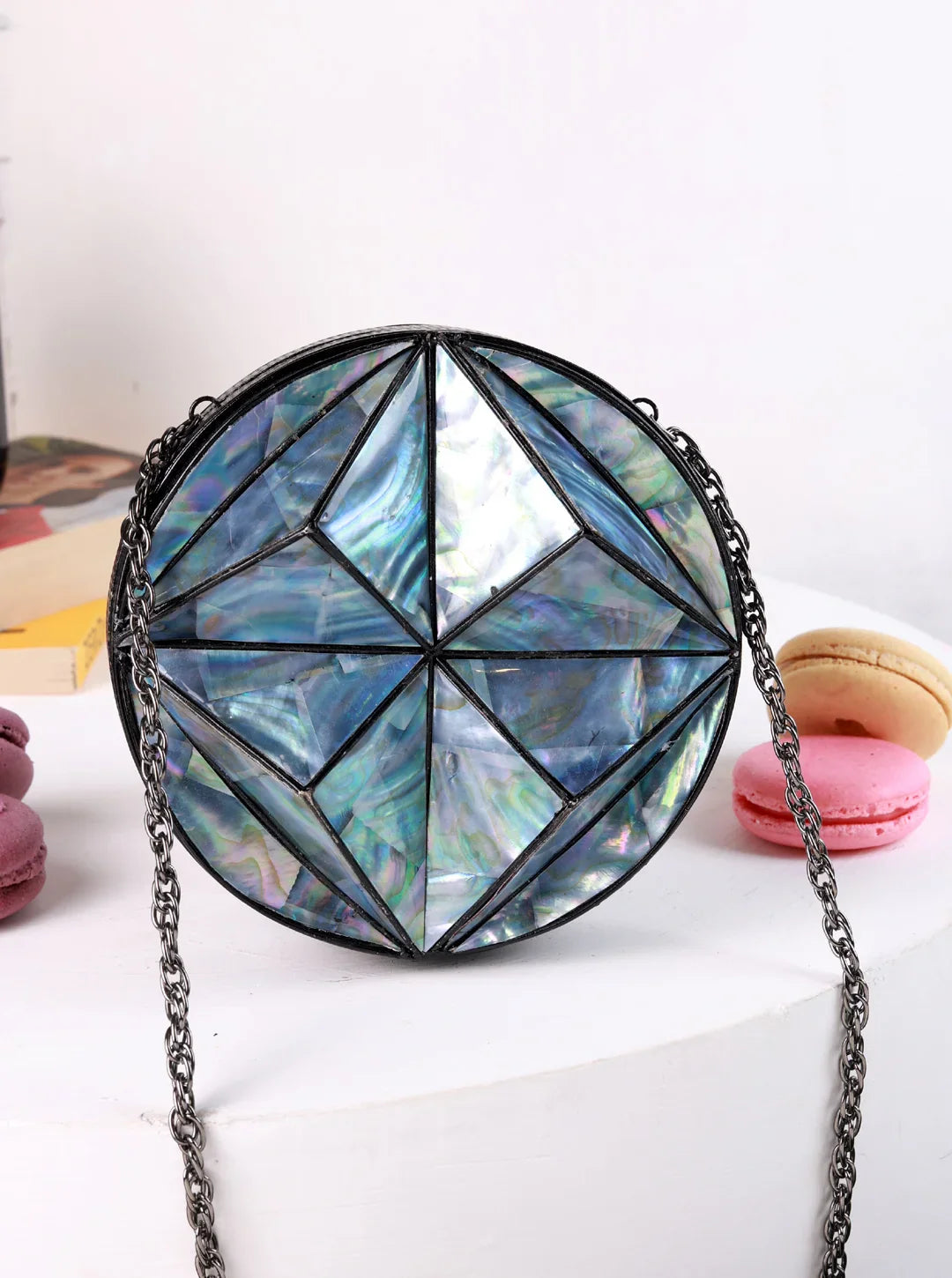 Geometrically patterned handbag with a chain strap on a white surface.