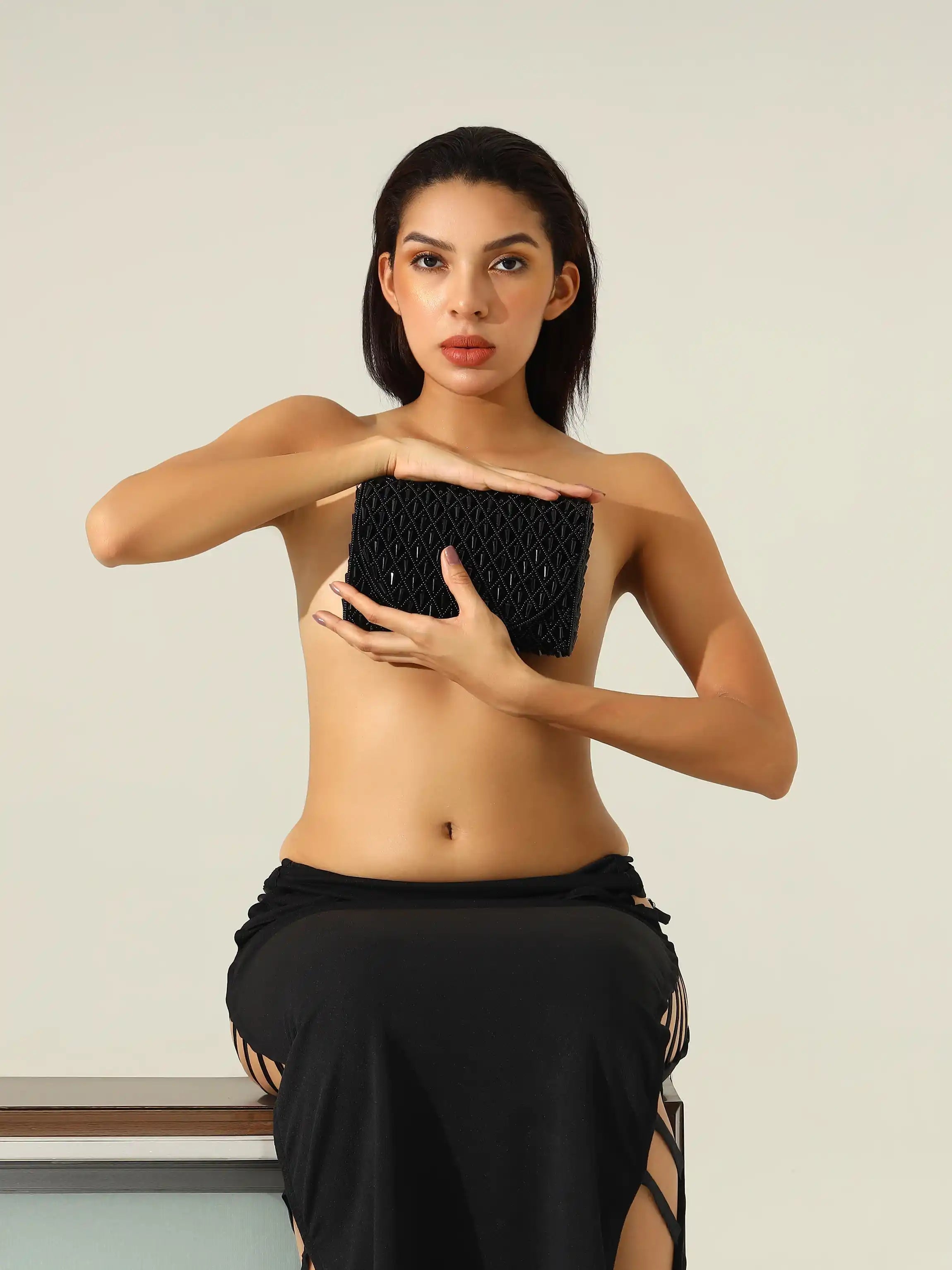Woman holding a black clutch against a plain background