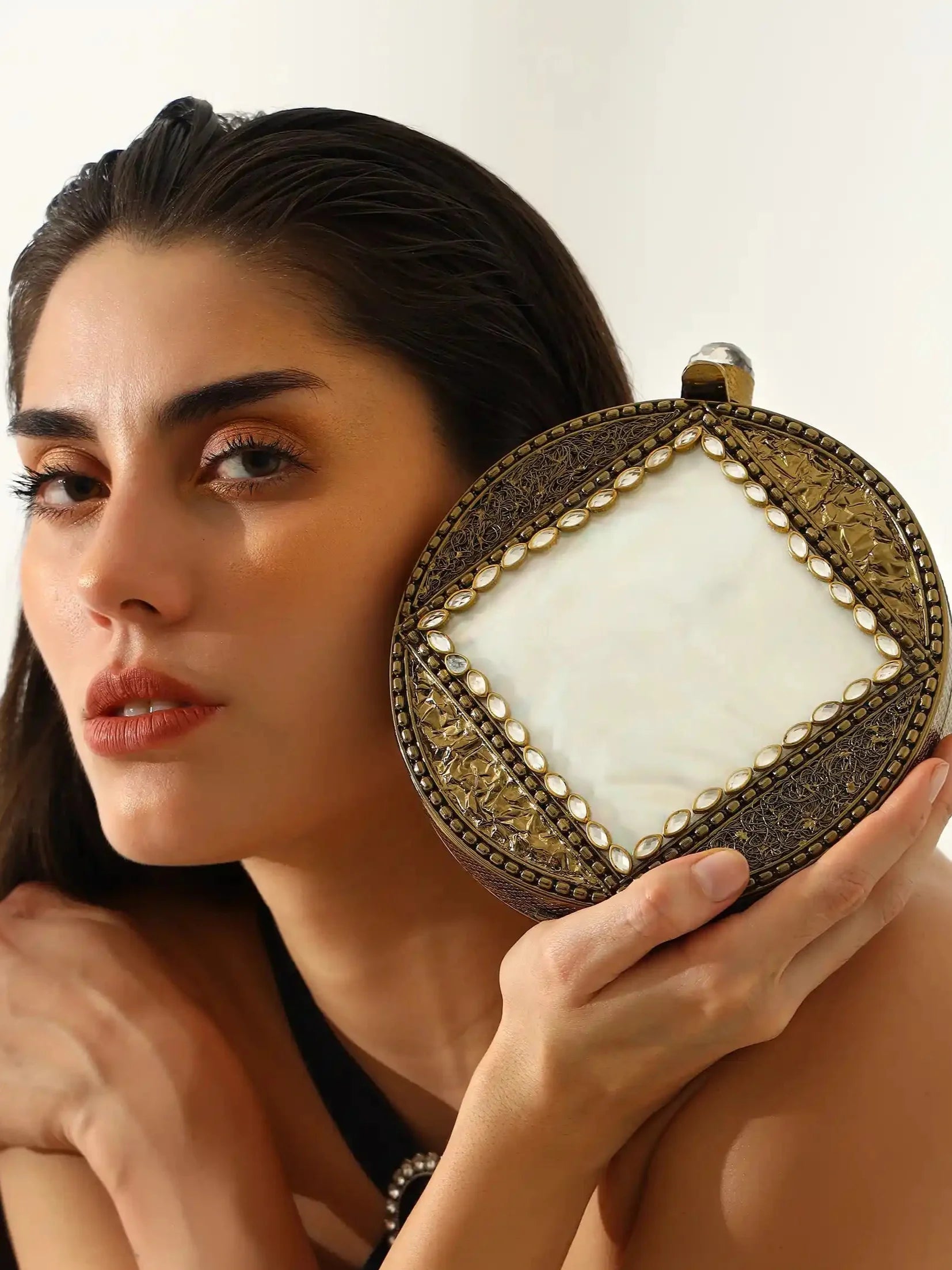 Woman holding a decorative clutch bag against a plain background
