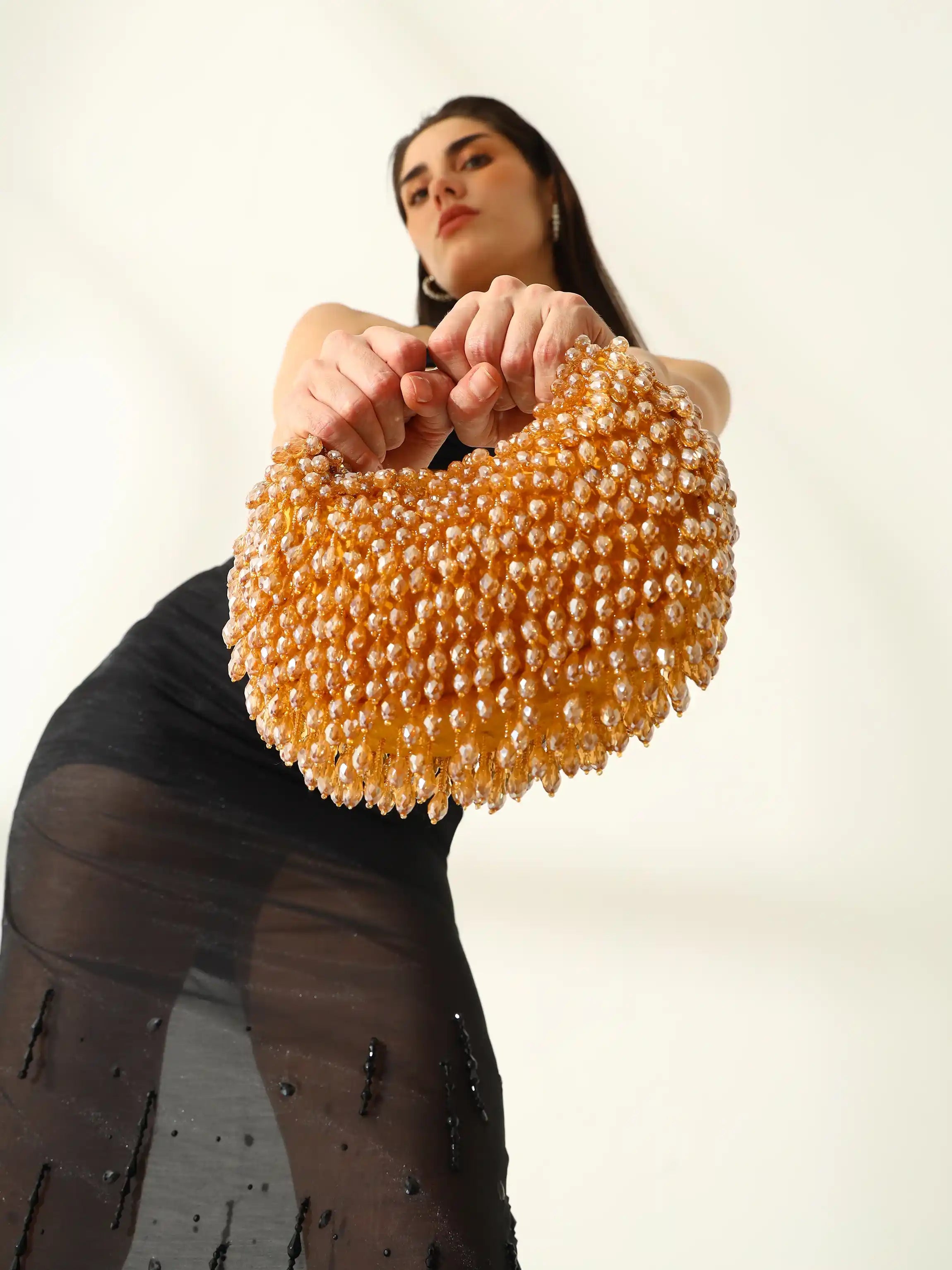 Woman holding a large yellow beaded clutch against a plain background
