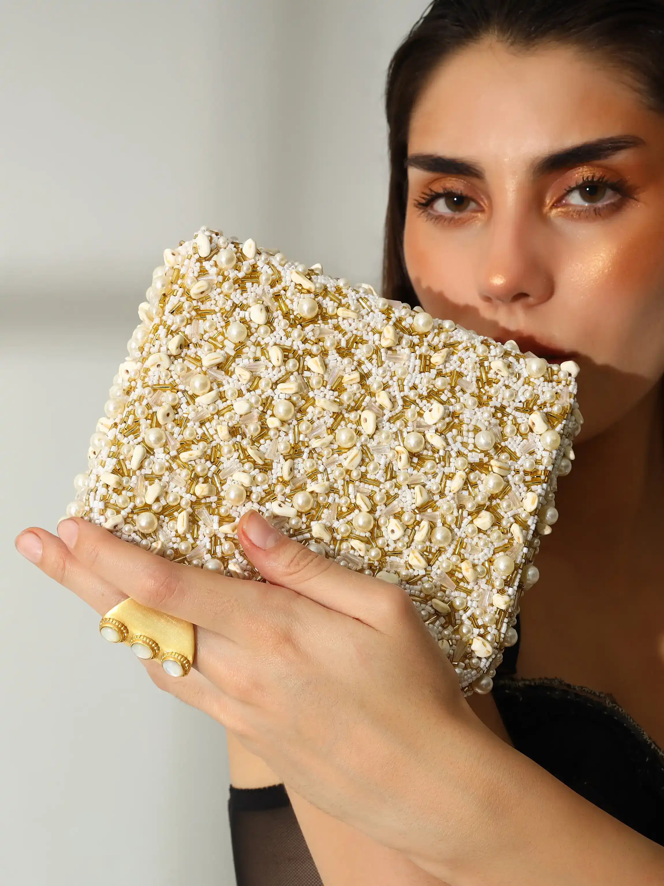 Woman holding a gold clutch with a textured surface against a neutral background