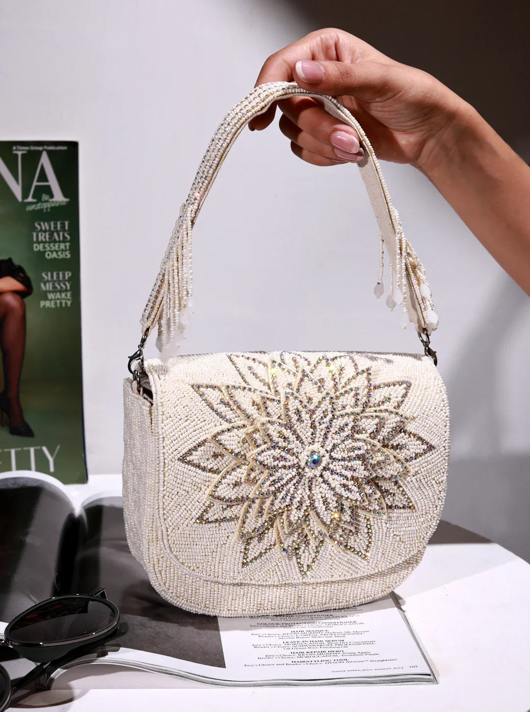 Handbag with decorative floral pattern held by a hand on a magazine background