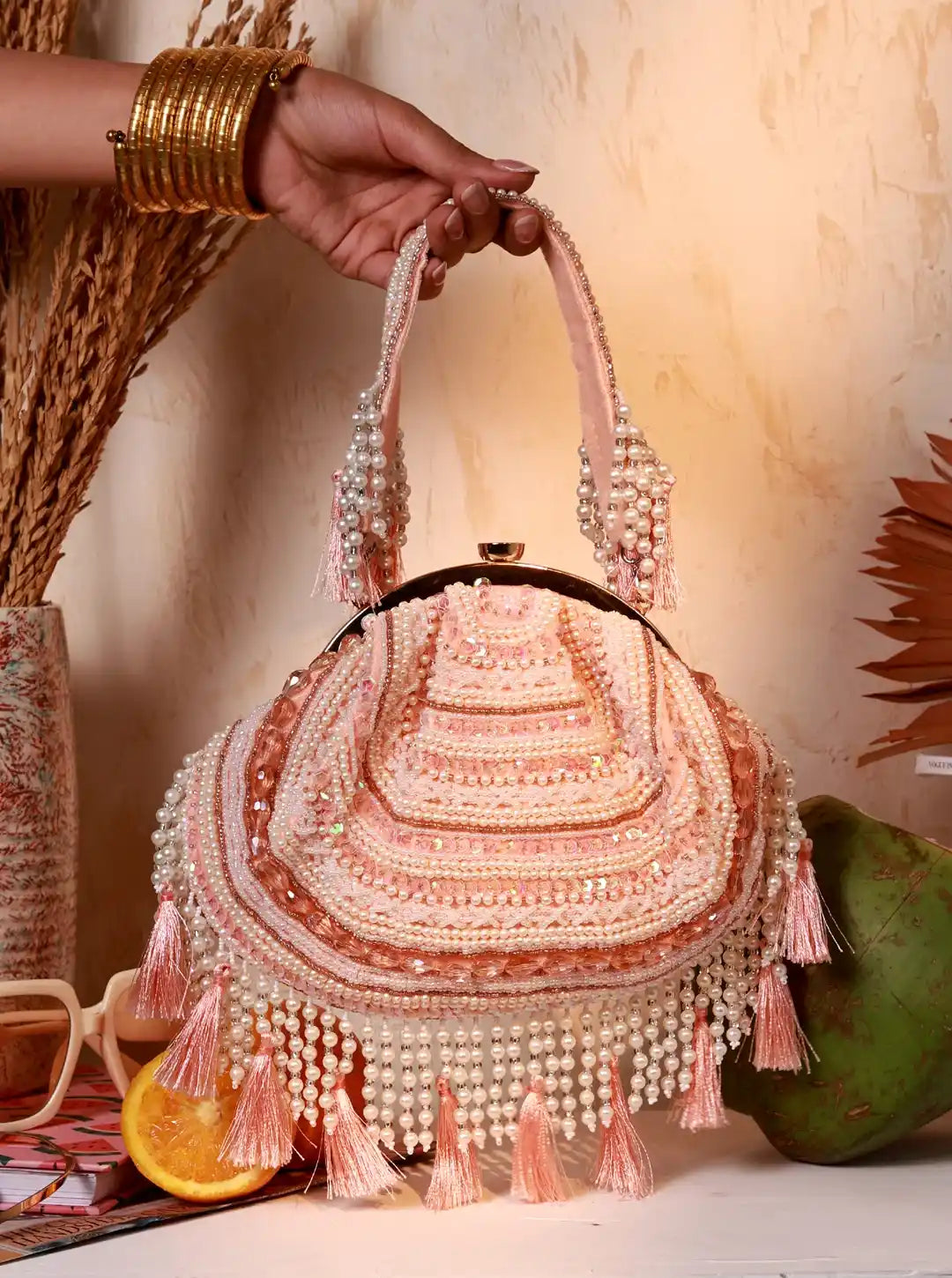 Decorative handbag with beads and tassels held by a hand against a warm-toned background.