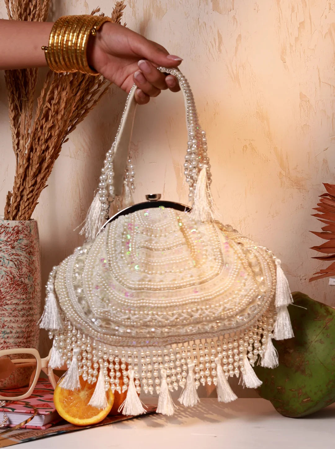 Handbag with beaded details held by a hand, with a decorative background