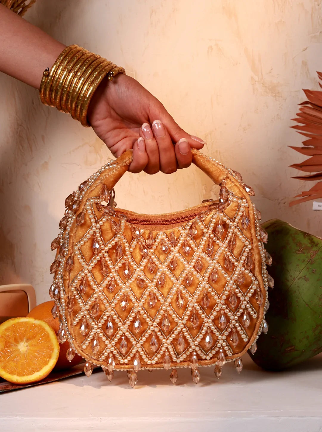 Hand holding a beaded handbag with a decorative pattern, surrounded by fruits on a light background.